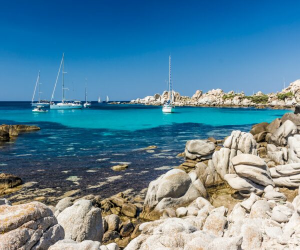 Photo of sailing boats anchored in a small cove in Corsica with beautiful clear water