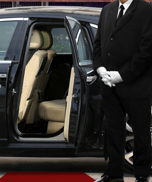 Private chauffeur waiting for guests in front of luxury vehicle