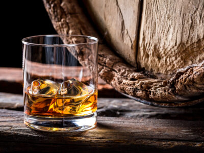 A glass of whisky in front of an old barrel