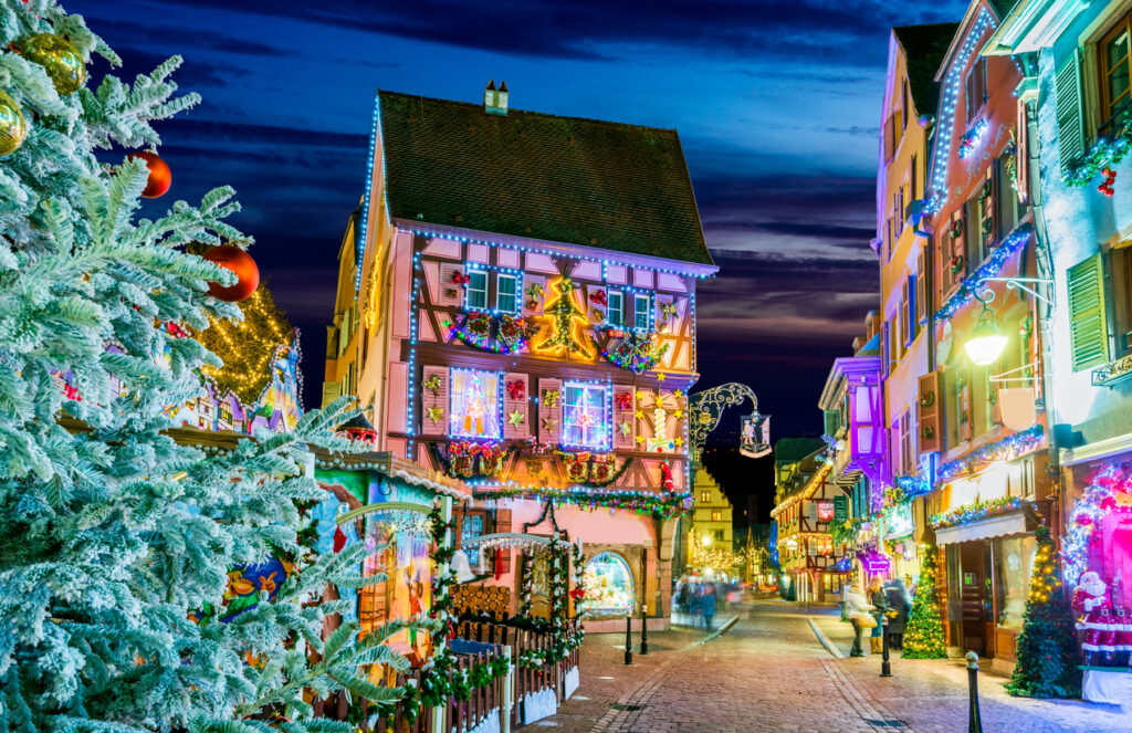 Charming Alsace village Christmas market in December featuring illuminated half-timbered houses, festive wooden chalets, holiday decorations, and a magical atmosphere where time seems to stand still.